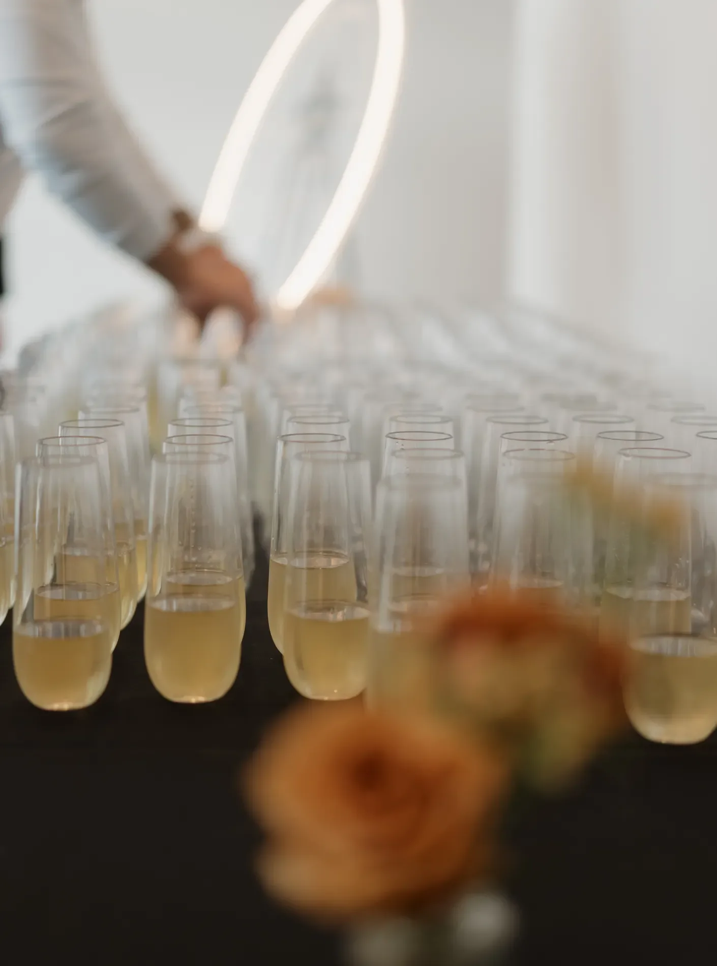 A hand placing a coupe on a champagne tower with peach roses in the foreground