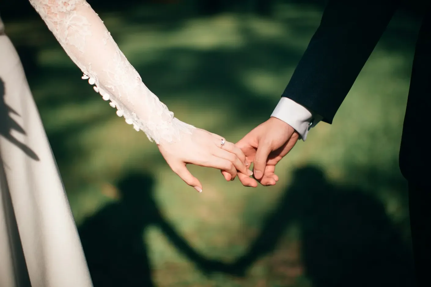 A couple reaching for each other’s hands, with lace and grass in the afternoon light